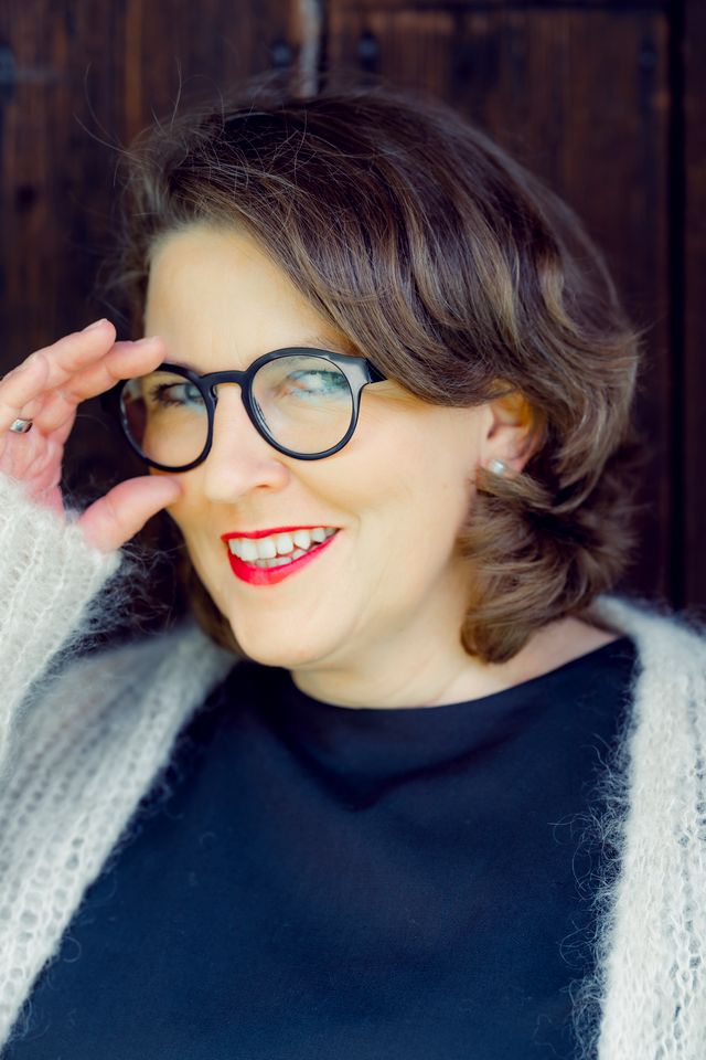 Portrait von Petra Reindl, Interim CFO in München, mit einer Hand an der Brille und lächelndem Gesicht